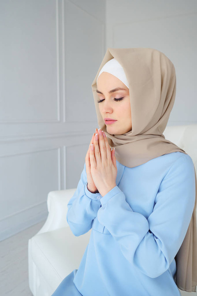 Bej tesettürlü ve geleneksel elbiseli genç müslüman kadın Allah için gözleri kapalı dua ediyor. - Fotoğraf, Görsel