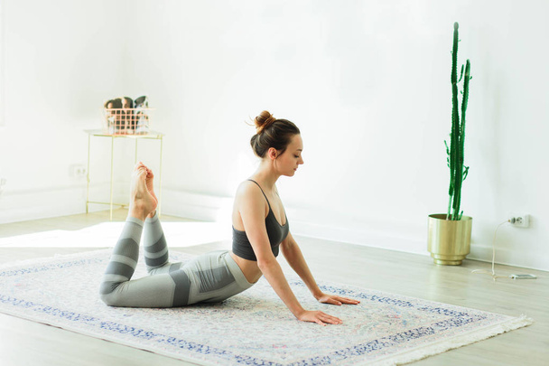 junge attraktive lächelnde Frau praktiziert Yoga in einem hellen Raum - Foto, Bild