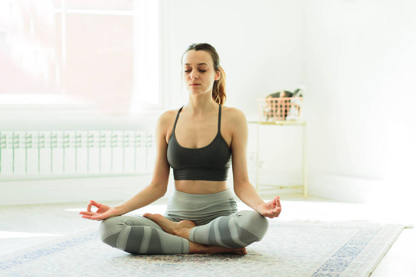 Mladý atraktivní usmívající se žena cvičit jógu v světlé místnosti - Fotografie, Obrázek