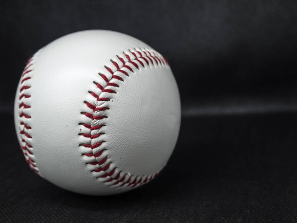 Pelota de béisbol con hilos rojos sobre un fondo oscuro
 - Foto, imagen