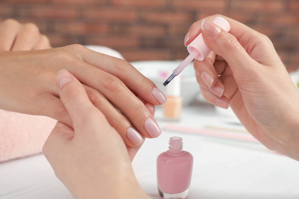 Manicurist applying polish on client's nails at table, closeup. Spa treatment - 写真・画像