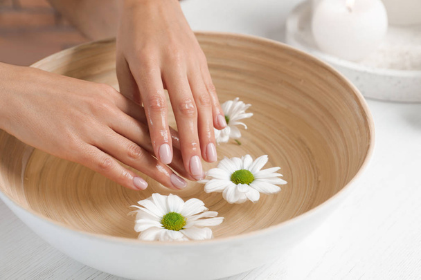 Woman soaking her hands in bowl with water and flowers on table, closeup. Spa treatment - Foto, Imagen