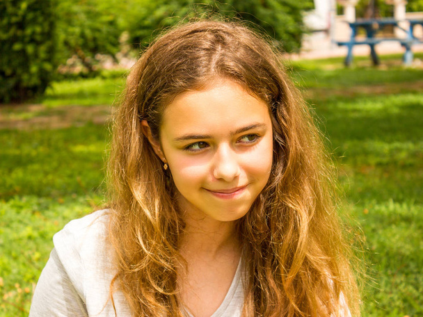 Hermosa chica adolescente con el pelo largo sonriendo en el parque en la hierba verde
 - Foto, imagen