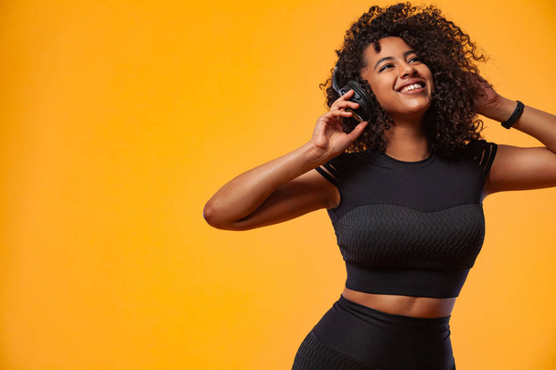 Lifestyle Concept. Portrait of beautiful African American woman with curly hair joyful listening to music on mobile phone. Yellow studio background. Copy Space. - Фото, изображение