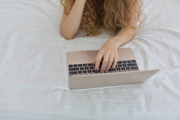 όμορφη ξανθιά γυναίκα που εργάζεται στο φορητό υπολογιστή, ενώ ξαπλωμένο στο κρεβάτι  - Φωτογραφία, εικόνα