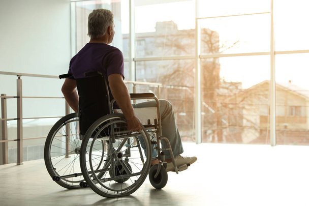 Senior man sitting in wheelchair near window at home - Fotó, kép