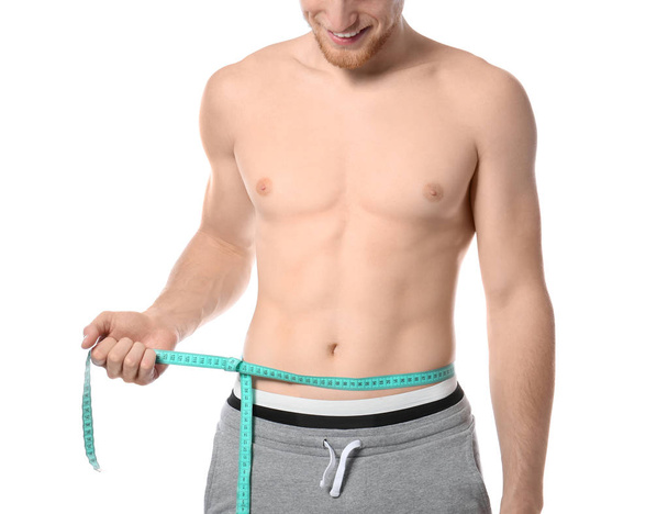 Young man with measuring tape showing his slim body on white background, closeup - 写真・画像