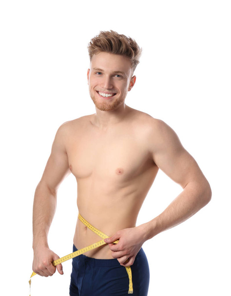 Portrait of young man with measuring tape showing his slim body on white background - Foto, afbeelding