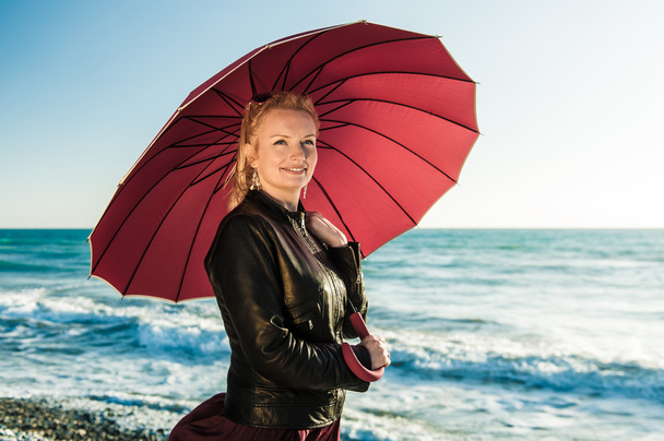 Девушка идет с красным зонтиком вдоль моря
 - Фото, изображение
