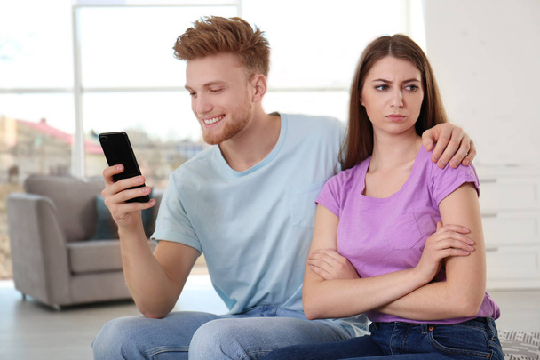 Young man engaged in smartphone while spending time with his girlfriend at home. Loneliness concept - Foto, Imagen