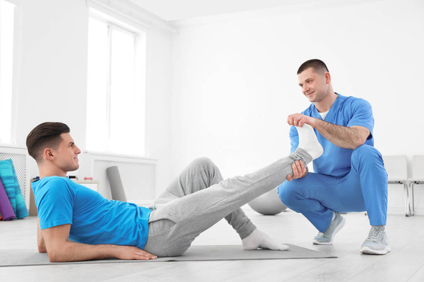Professional physiotherapist working with male patient in rehabilitation center - Фото, изображение