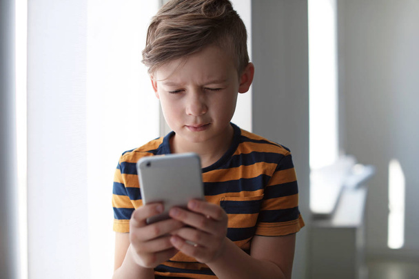 Sad little child with smartphone indoors. Danger of internet - Фото, зображення