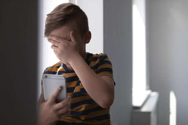 Frightened little child with smartphone indoors. Danger of internet - Φωτογραφία, εικόνα