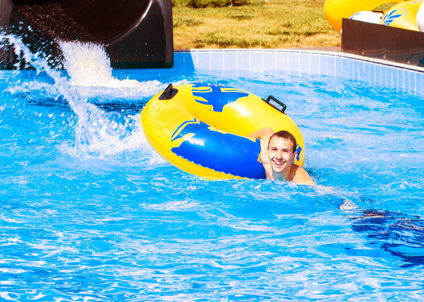 Смішний збуджений чоловік насолоджується літнім відпочинком у аквапарку, катаючись на жовтому плаву сміється
. - Фото, зображення