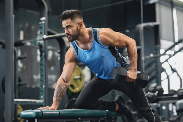 Handsome athlete working out with dumbbell at gym - Photo, Image