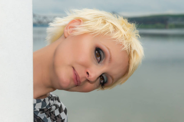 Krásný portrét bělošské bílé dívky s krátkými blondími vlasy ve venkovním prostředí. Zakoušené oči. Technika řezu.  - Fotografie, Obrázek