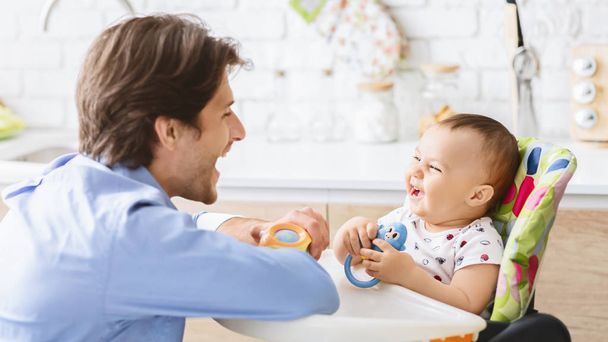 台所で彼の赤ちゃんの息子と笑うミレニアルの男 - 写真・画像