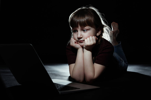 Little child in front of laptop on dark background. Cyber danger - Photo, Image