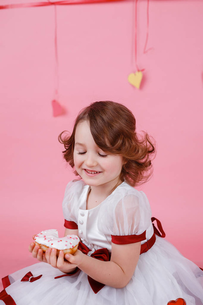Portrét malé holčičky s koblihu v dlaních na růžovém pozadí - Fotografie, Obrázek