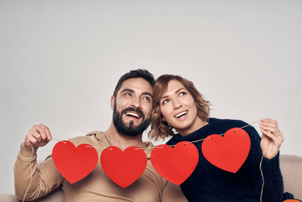 Smiling couple sitting on sofa holding four heart shape garland - Foto, imagen