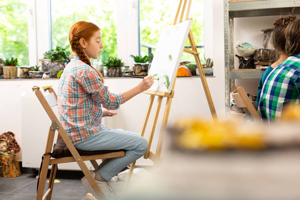 Talented girl sitting near drawing easel and coloring picture - 写真・画像