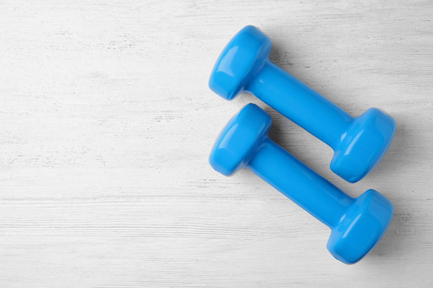 Bright dumbbells and space for text on wooden background, flat lay. Home fitness - 写真・画像