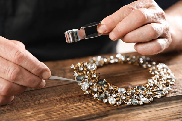 Male jeweler evaluating necklace at table in workshop, closeup - 写真・画像