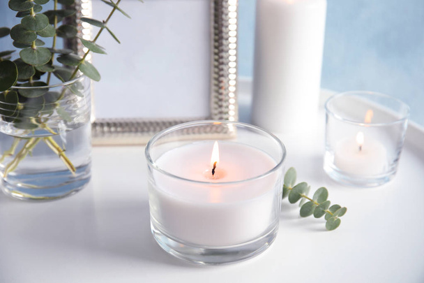 Burning aromatic candle and eucalyptus branch on table - Foto, afbeelding
