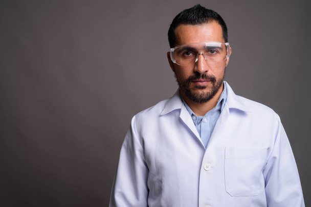 Στιγμιότυπο του όμορφου γενειοφόρου Πέρση γιατρό φορώντας προστατευτικά γυαλιά σε γκρι φόντο - Φωτογραφία, εικόνα
