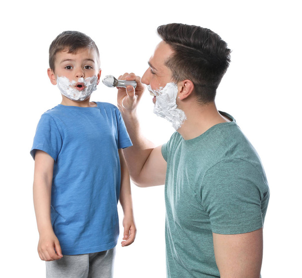 Dad applying shaving foam onto son's face against white background - Photo, Image