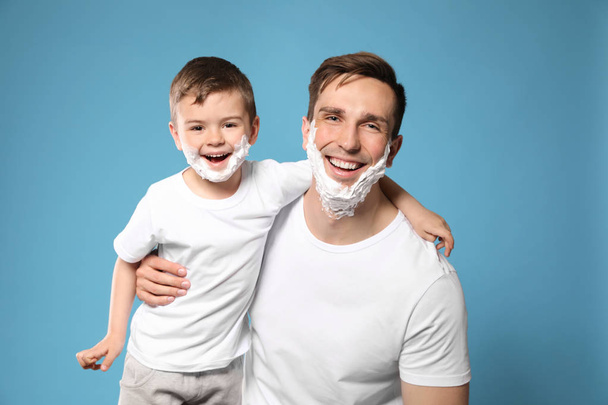Dad and his little son with shaving foam on faces against color background - Foto, Imagen