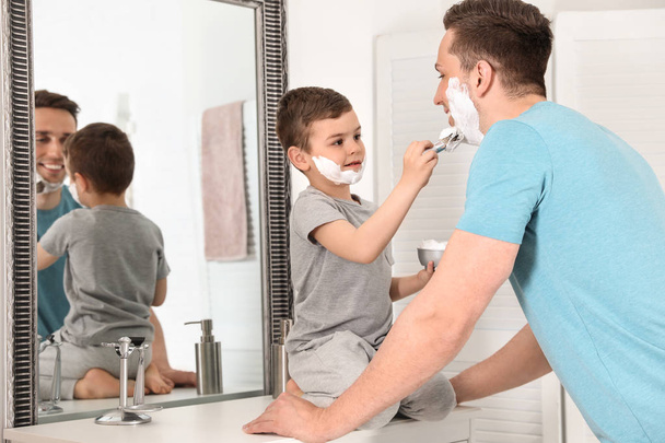 Little son applying shaving foam onto dad's face in bathroom - Foto, Imagen