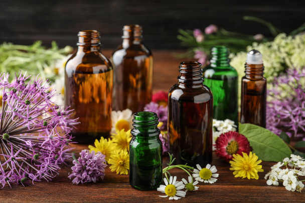 Diferentes garrafas de óleos essenciais e flores na mesa
 - Foto, Imagem