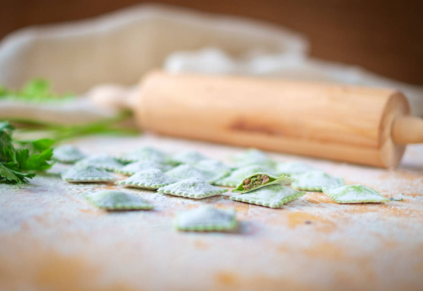 traditional raw ravioli with spinach and meat on a wooden table with flour, handmade, cooking process - Foto, Imagem