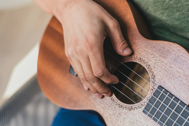 ukelele spel. een man die een kleine gitaar speelt. de performer schrijft de muziek op de ukulele thuis. - Foto, afbeelding
