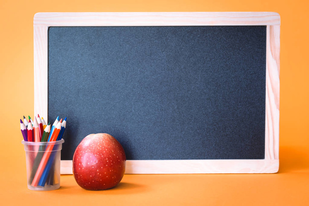 Manzana con lápices y pizarra escolar sobre fondo naranja
 - Foto, Imagen