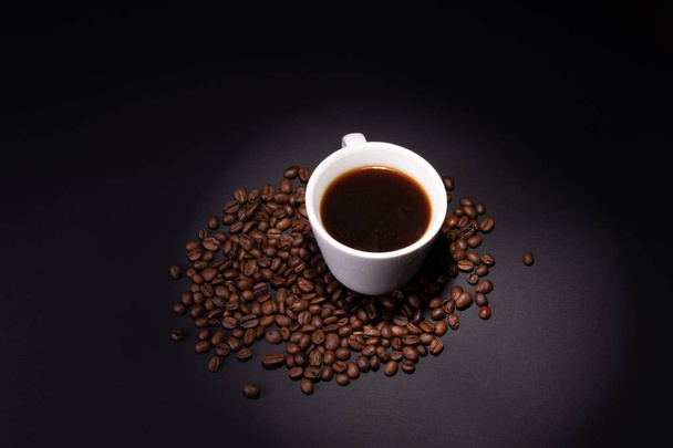 A cup of brewed coffee among the coffee beans on a dark surface - Фото, зображення