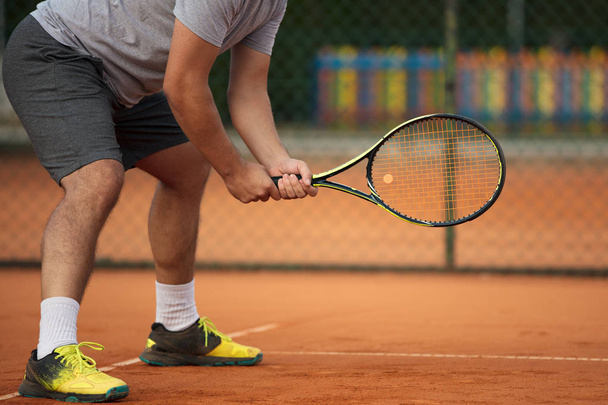 Close up of man holding tennis racket on clay court. On court is sunset. Man holding tennis racket - Фото, изображение