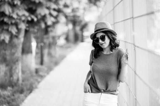 Young pretty brunette walking around the city on a sunny day, dressed in summer clothes, and a hat on her head. Summer style - Fotoğraf, Görsel