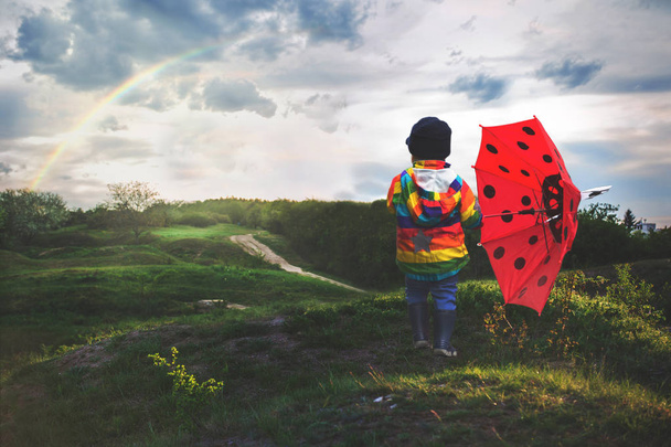 Beautiful toddler boy with rainbow raincoat, enjoying the rain,  - Foto, Imagen