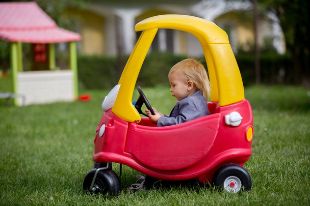 Lindo niño pequeño, montar gran juguete de plástico coche rojo en el parque
 - Foto, imagen