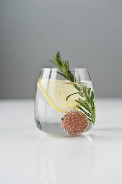 glass of clear water with lemon, rosemary, lychee. - Foto, Bild