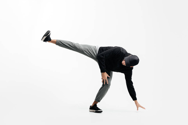 Handsome young man wearing a black sweatshirt, gray pants and a cap is dancing breakdance - 写真・画像