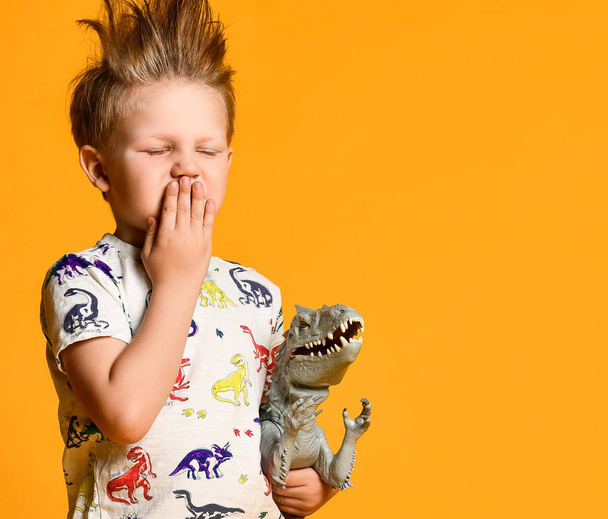 little boy with a funny, disheveled hair holds the toy plastic dinosaur as a portrait. - Fotoğraf, Görsel