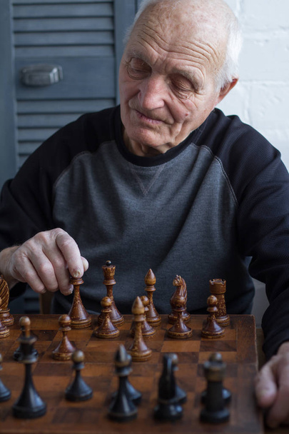 ein alter Mann sitzt vor einem Schachbrett, denkt nach und macht den ersten Zug im Spiel - Foto, Bild