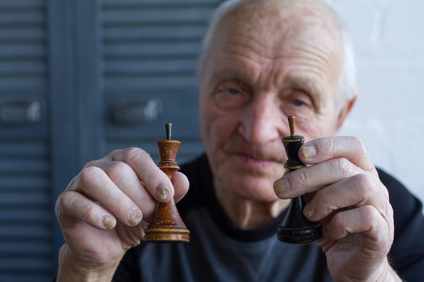 Ο γέρος κρατά στα χέρια του το κομμάτι του σκακιού του βασιλιά, την έννοια της νίκης ή της απώλειας - Φωτογραφία, εικόνα