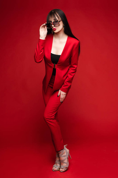 Πλευρική όψη του λαμπερή μελαχρινή που ποζάρει με κόκκινο έξυπνο κοστούμι - Φωτογραφία, εικόνα