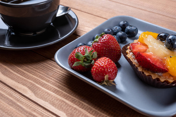 fruit tartlets on a wooden plate and cup of coffee on the table, - Photo, Image