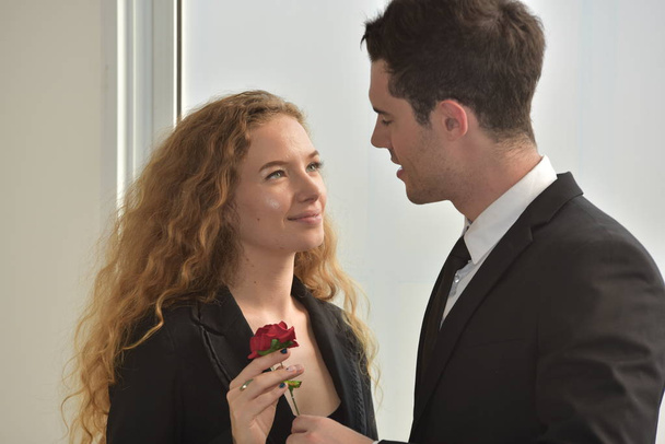 Επιχειρηματίας δίνοντας κόκκινο λουλούδι στην επιχειρηματία, υπόθεση στο χώρο εργασίας. - Φωτογραφία, εικόνα