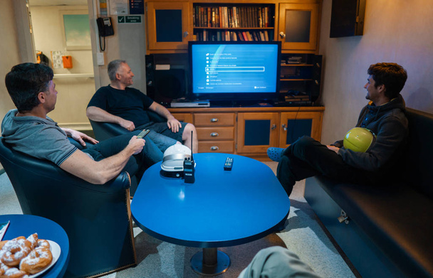 Счастливая команда корабельных офицеров смотрит телевизор на борту судна
 - Фото, изображение